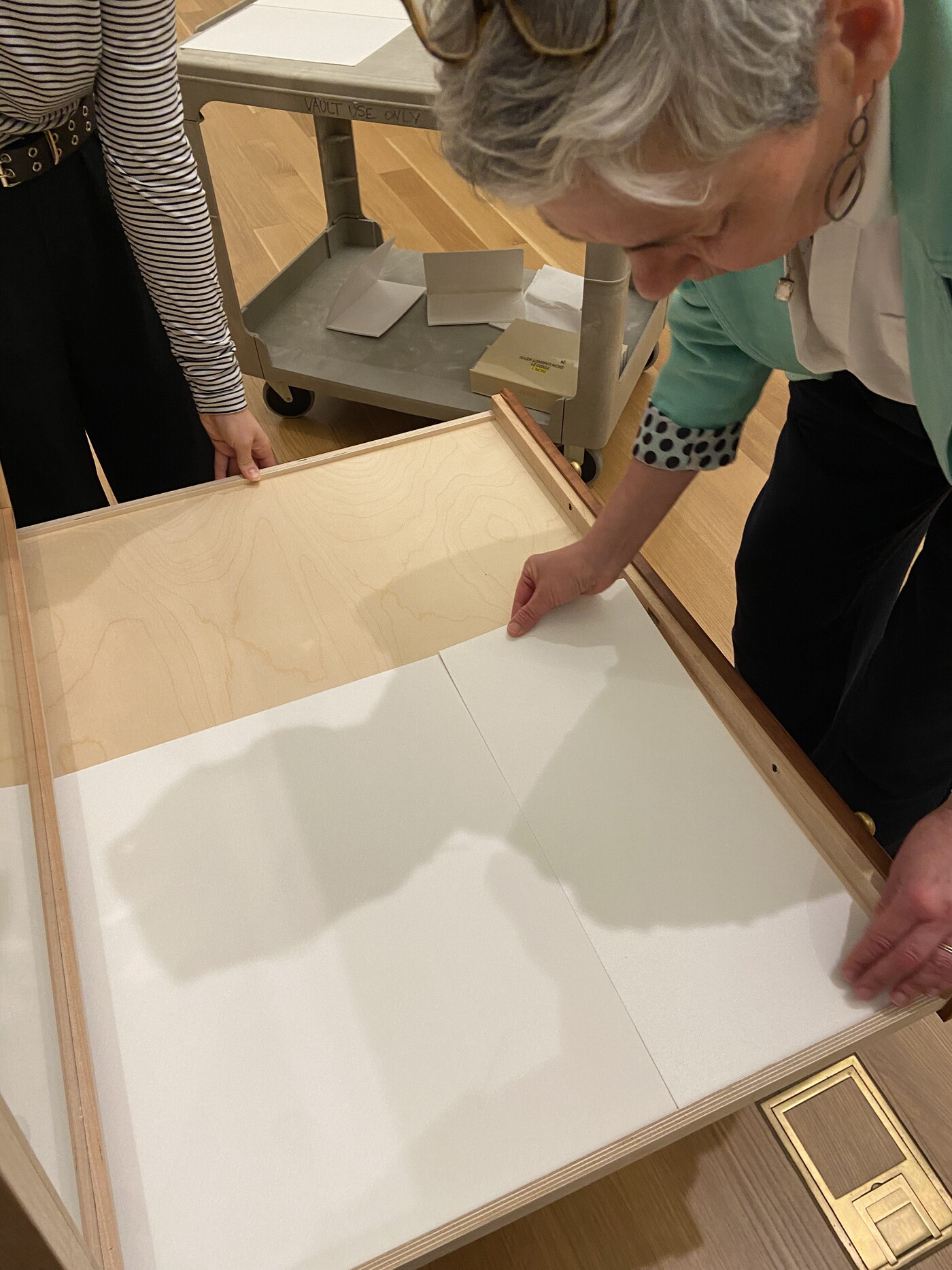 A woman leans over a drawer in a wood cabinet carefully placing a white sheet.