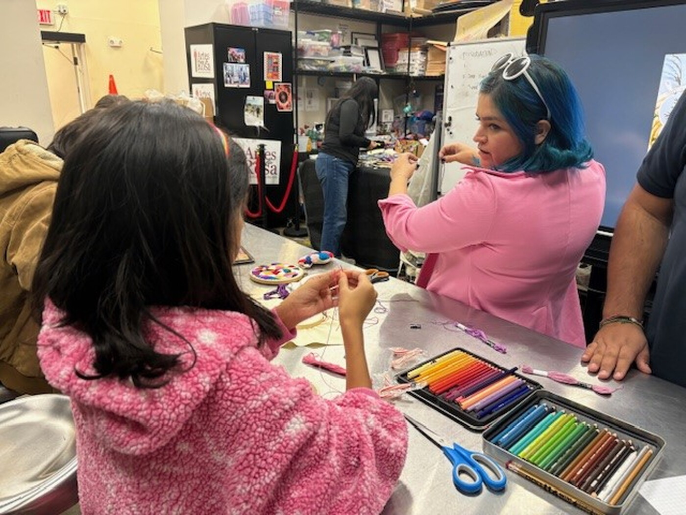 A woman demonstrates to several teens techniques for sewing.