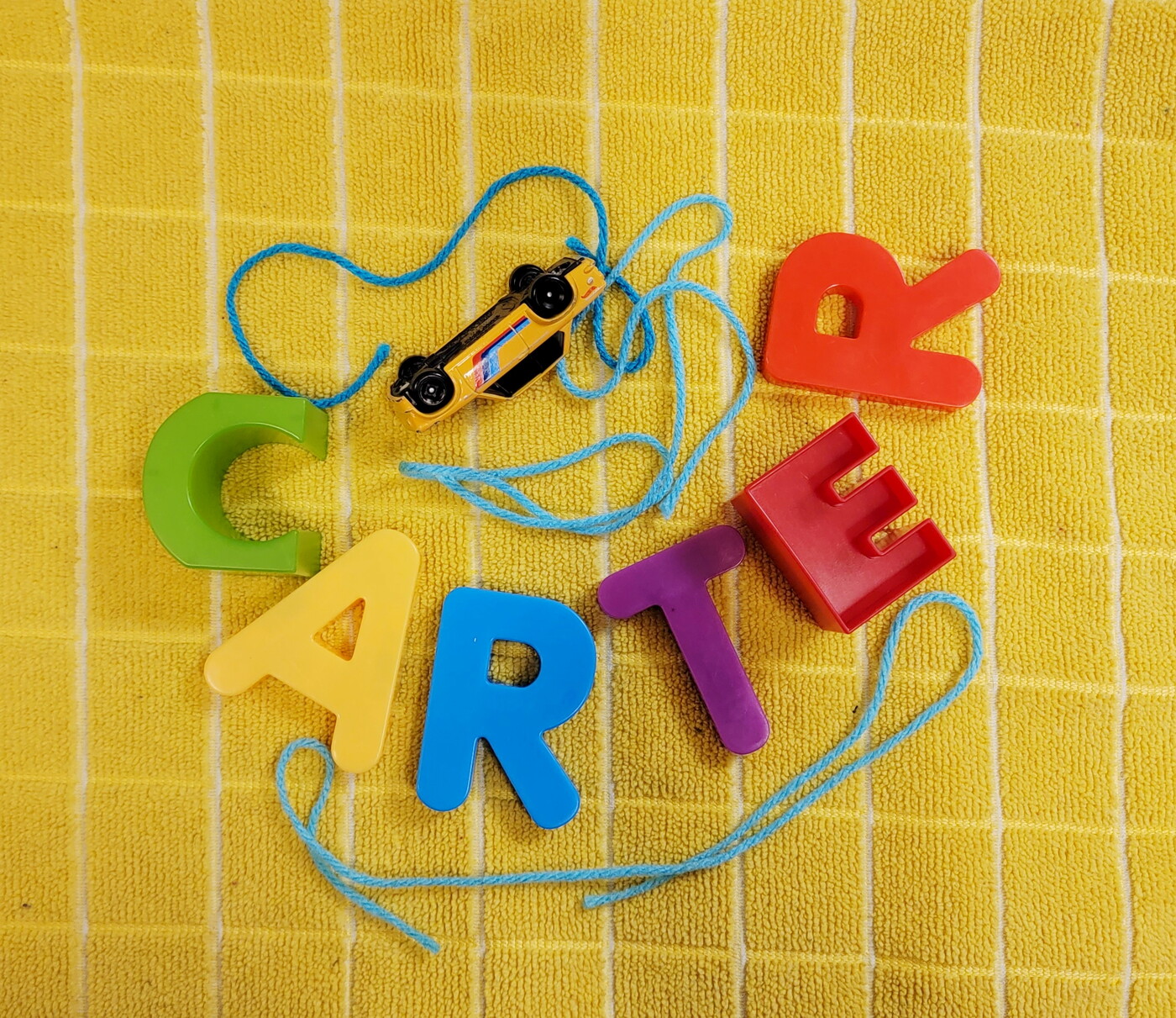 A piece of string, a toy car, and magnetic letters that spell "CARTER" arranged on a yellow towel.