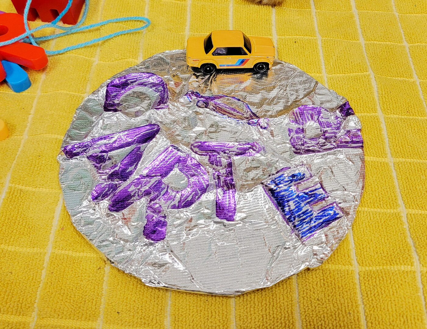 A circular foil artwork with colored impressions of letters lays on a table.