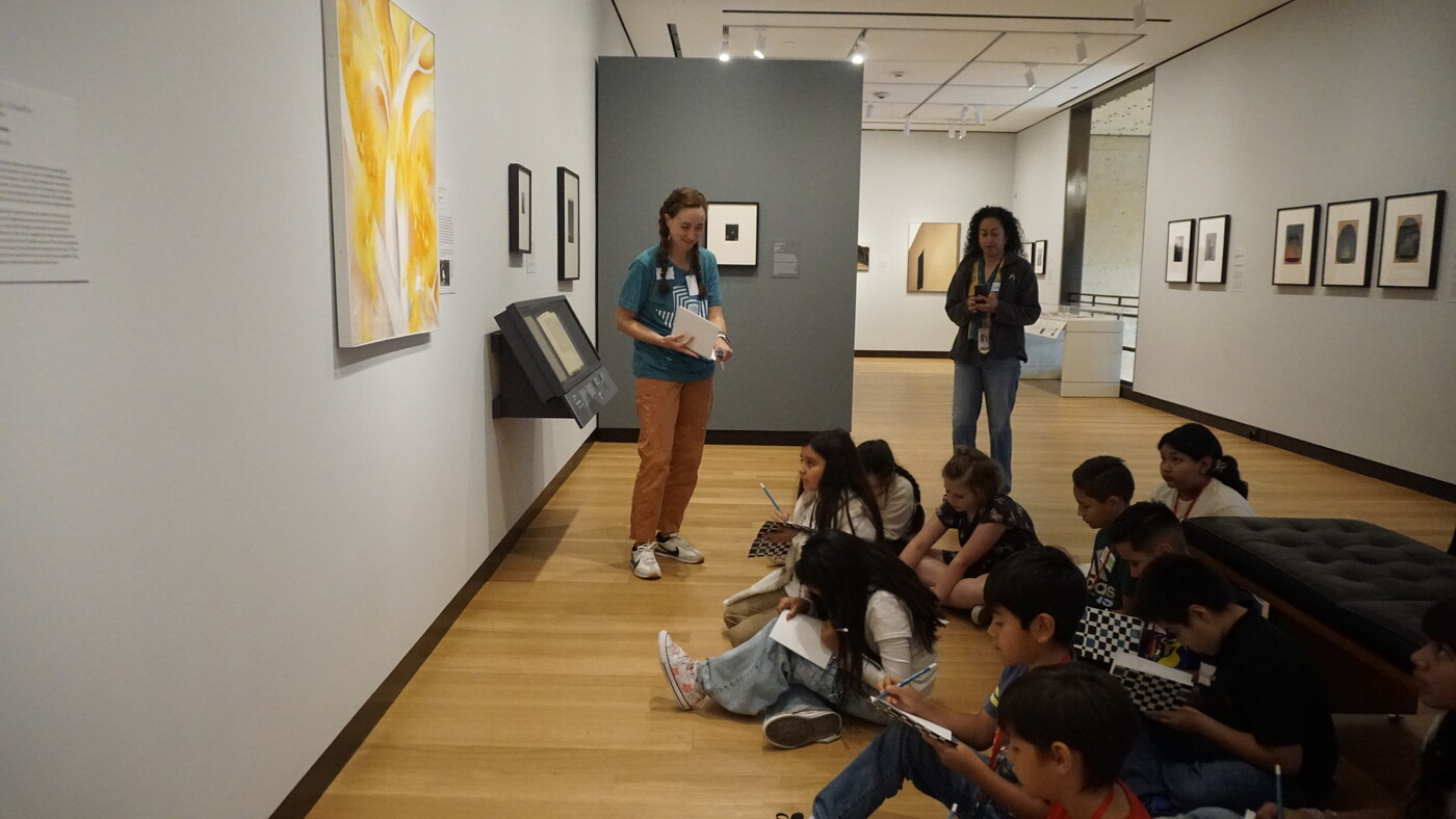 A Carter educator talks to a group of students who are sketching on the floor of a Carter gallery.