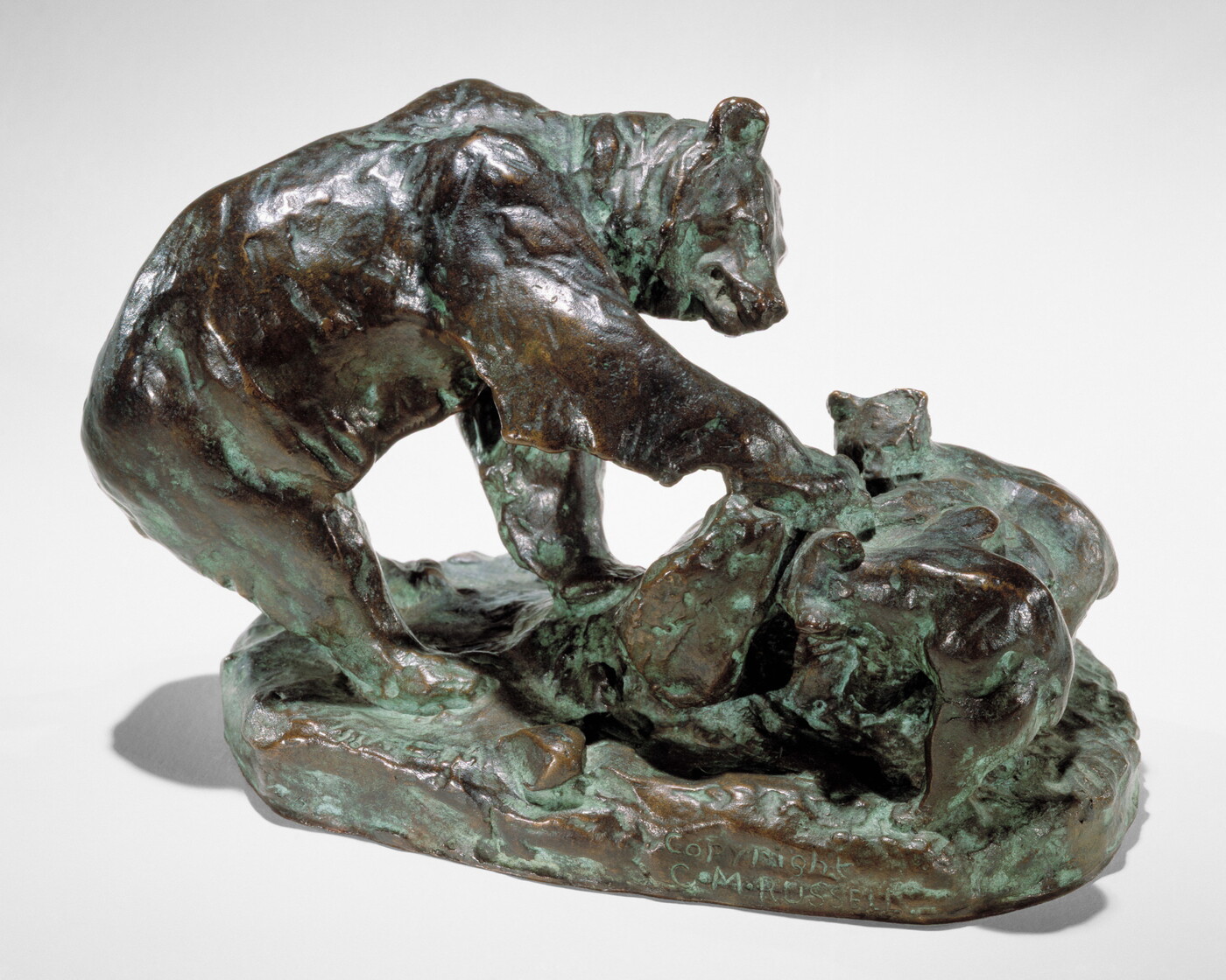A bronze sculpture of a bear and its cub pawing an upturned rock.