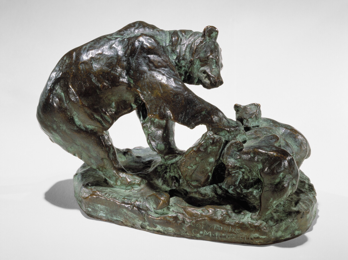 A bronze sculpture of a bear and its cub pawing an upturned rock.