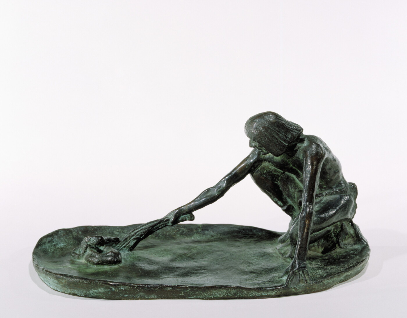 A bronze sculpture of a squatting Indigenous man holding a stick in his outstretched arm toward a snake on the ground.