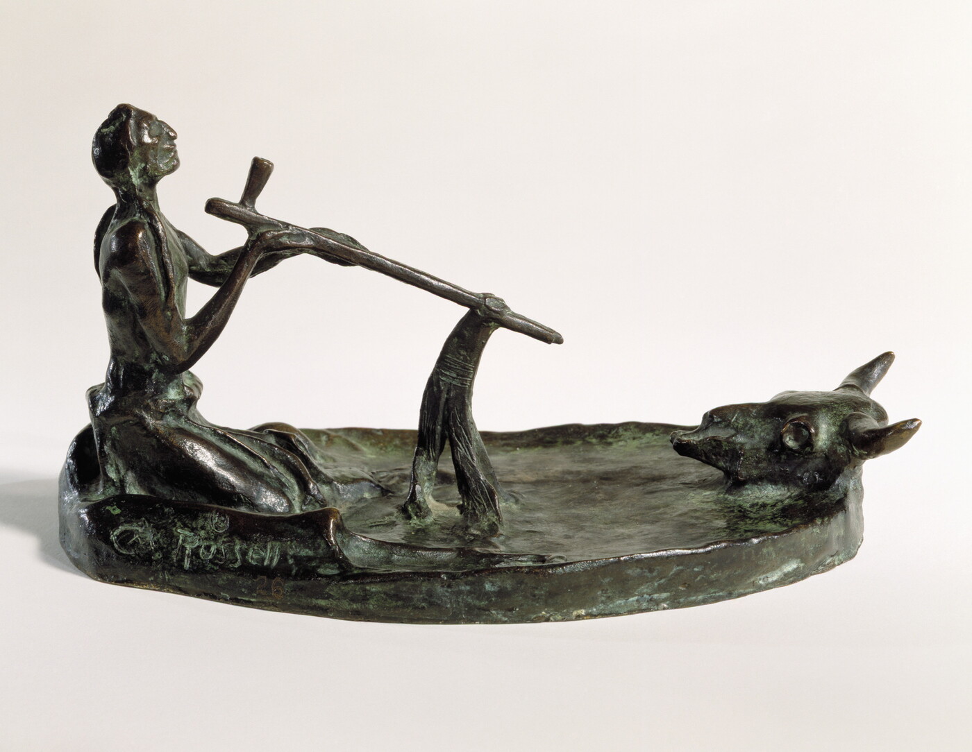 A bronze sculpture of a kneeling Native American man smoking a pipe in front of a bison skull.