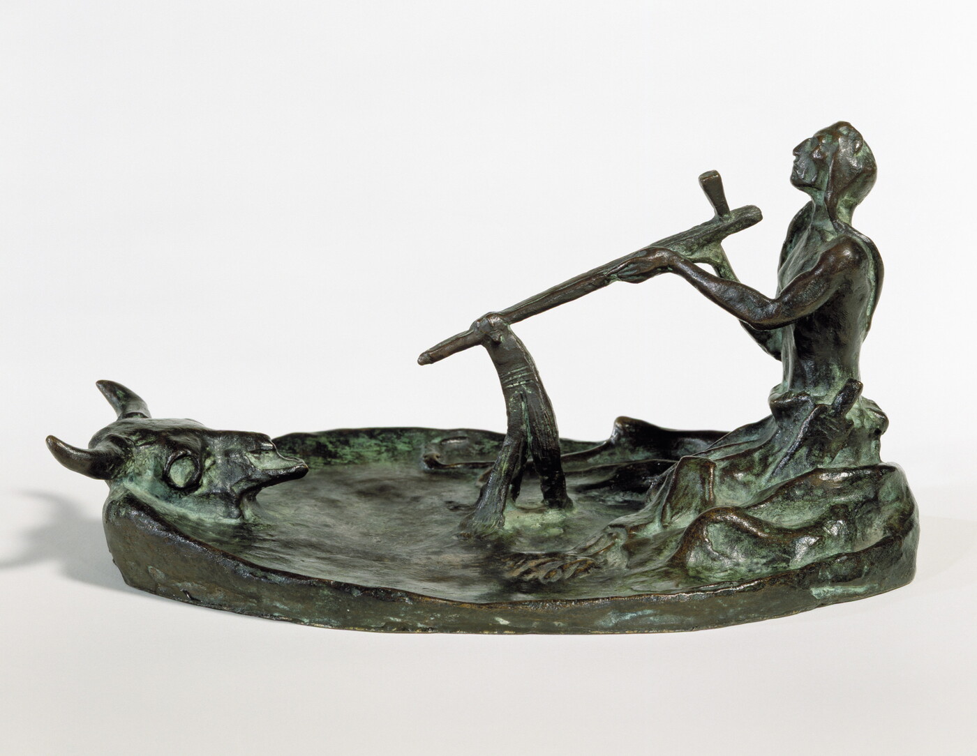 A bronze sculpture of a kneeling Native American man smoking a pipe in front of a bison skull.
