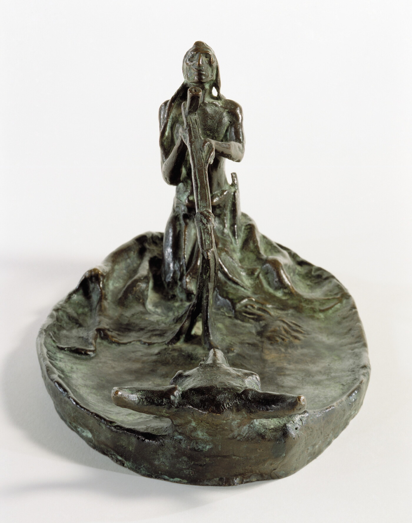 A bronze sculpture of a kneeling Native American man smoking a pipe in front of a bison skull.