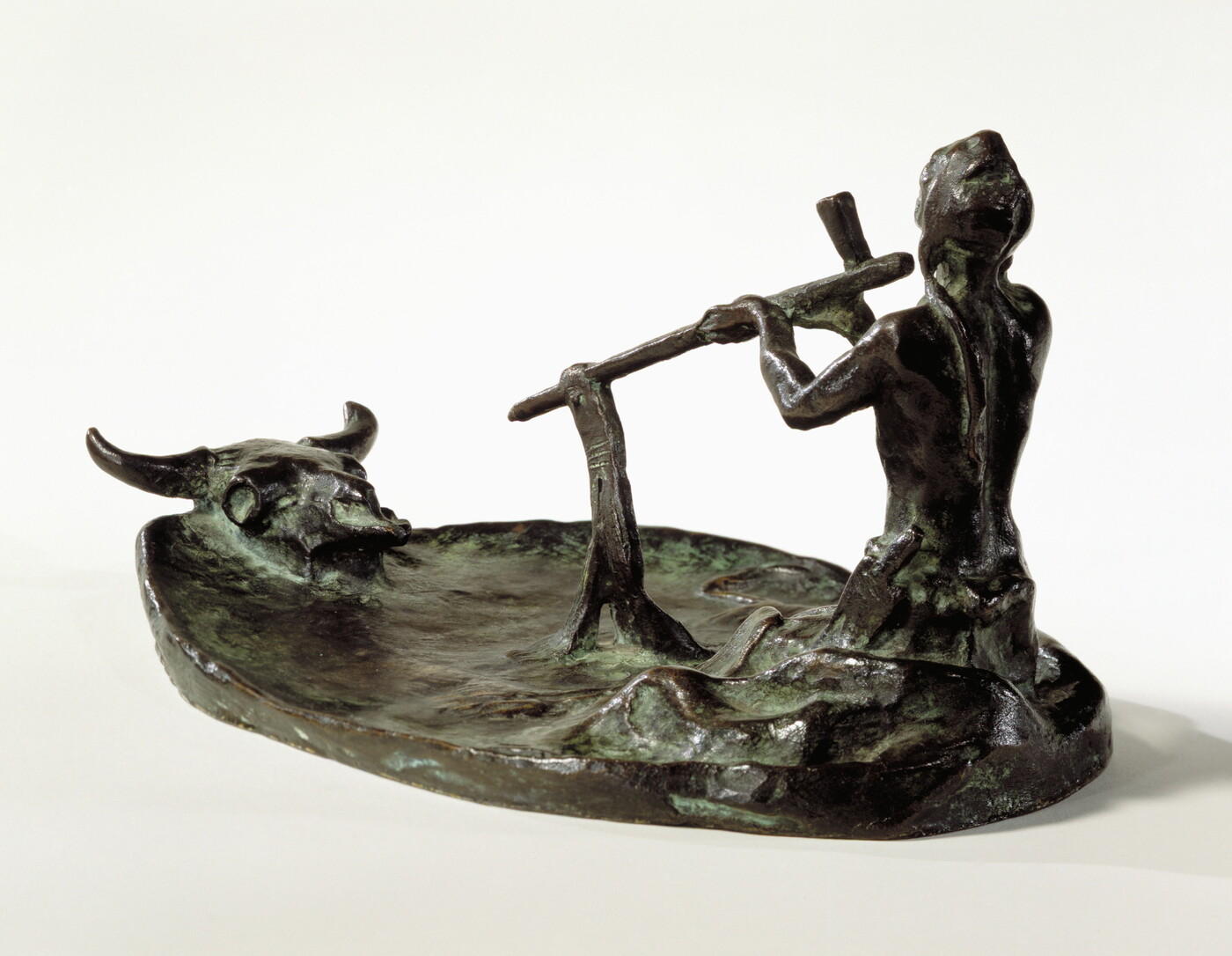 A bronze sculpture of a kneeling Native American man smoking a pipe in front of a bison skull.