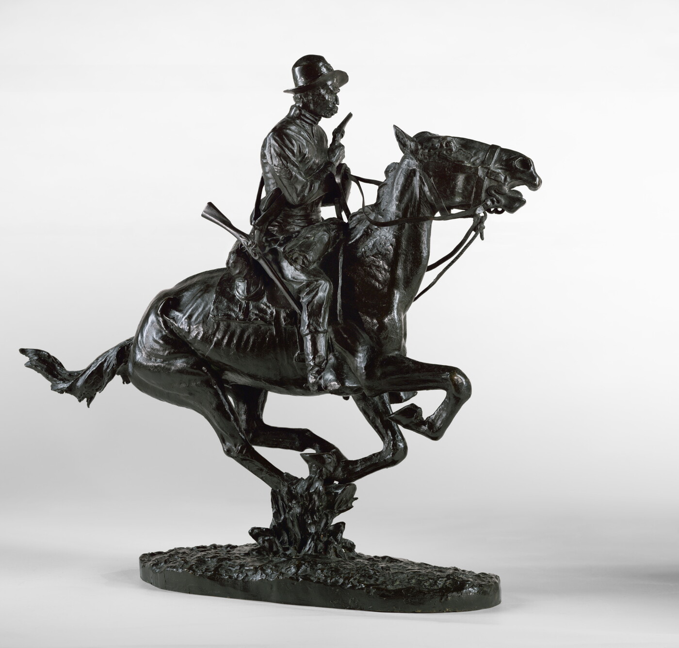 A bronze sculpture of a cowboy riding a galloping horse and holding a pistol close to his chest.