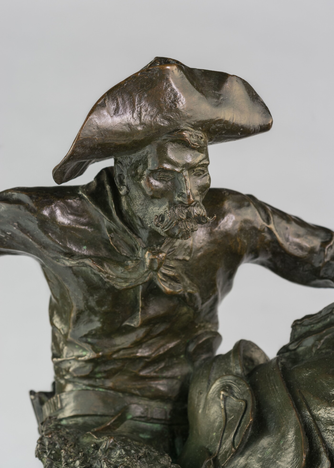 A detail of bronze sculpture of a cowboy balancing on a rearing horse.