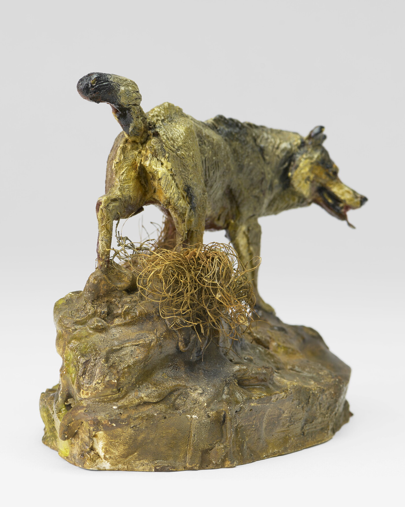 A painted sculpture of a wolf walking across patches of grass on a rock.