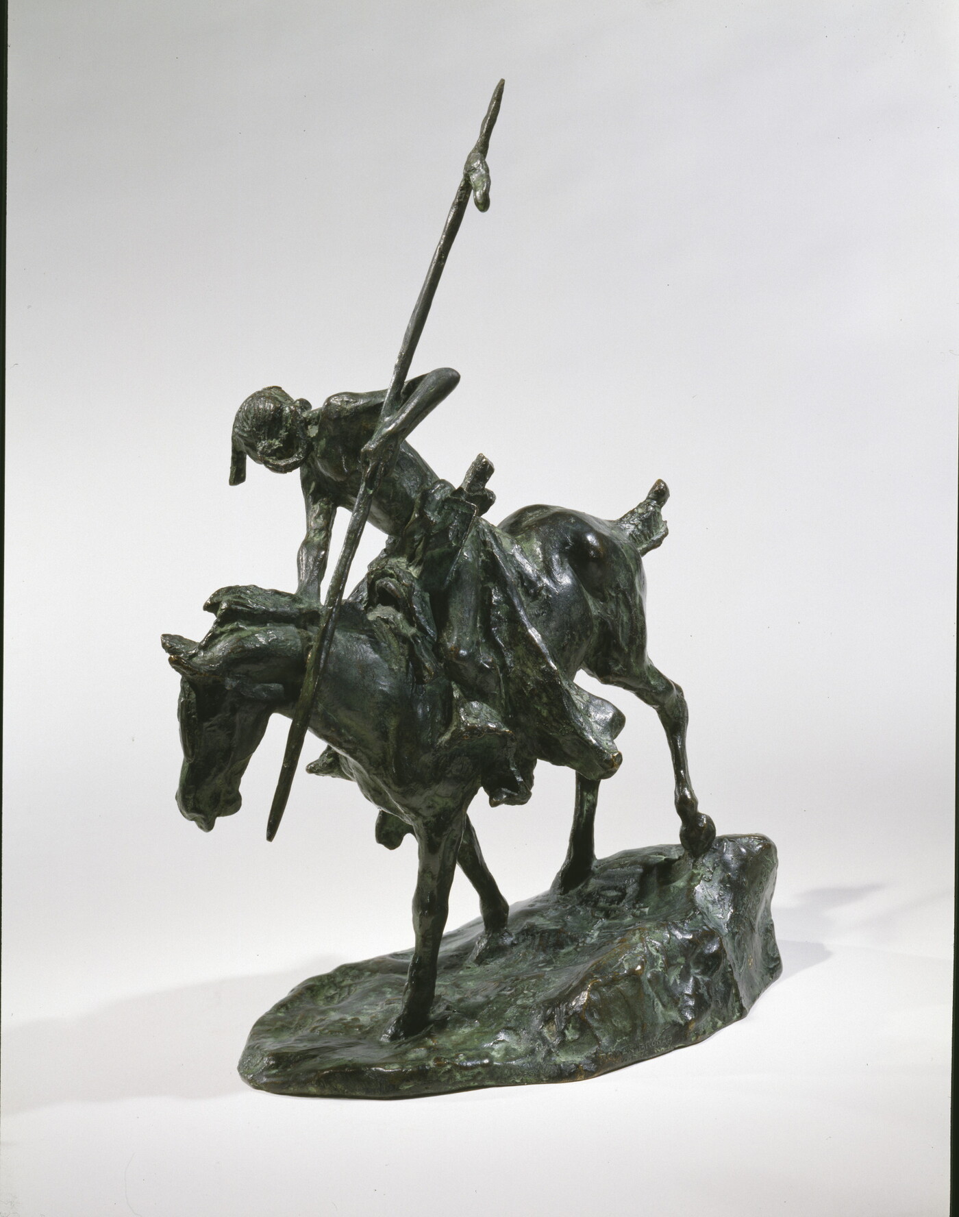 A bronze sculpture of an Indigenous man on horseback holding a spear pointed toward the ground as he studies footprints there.