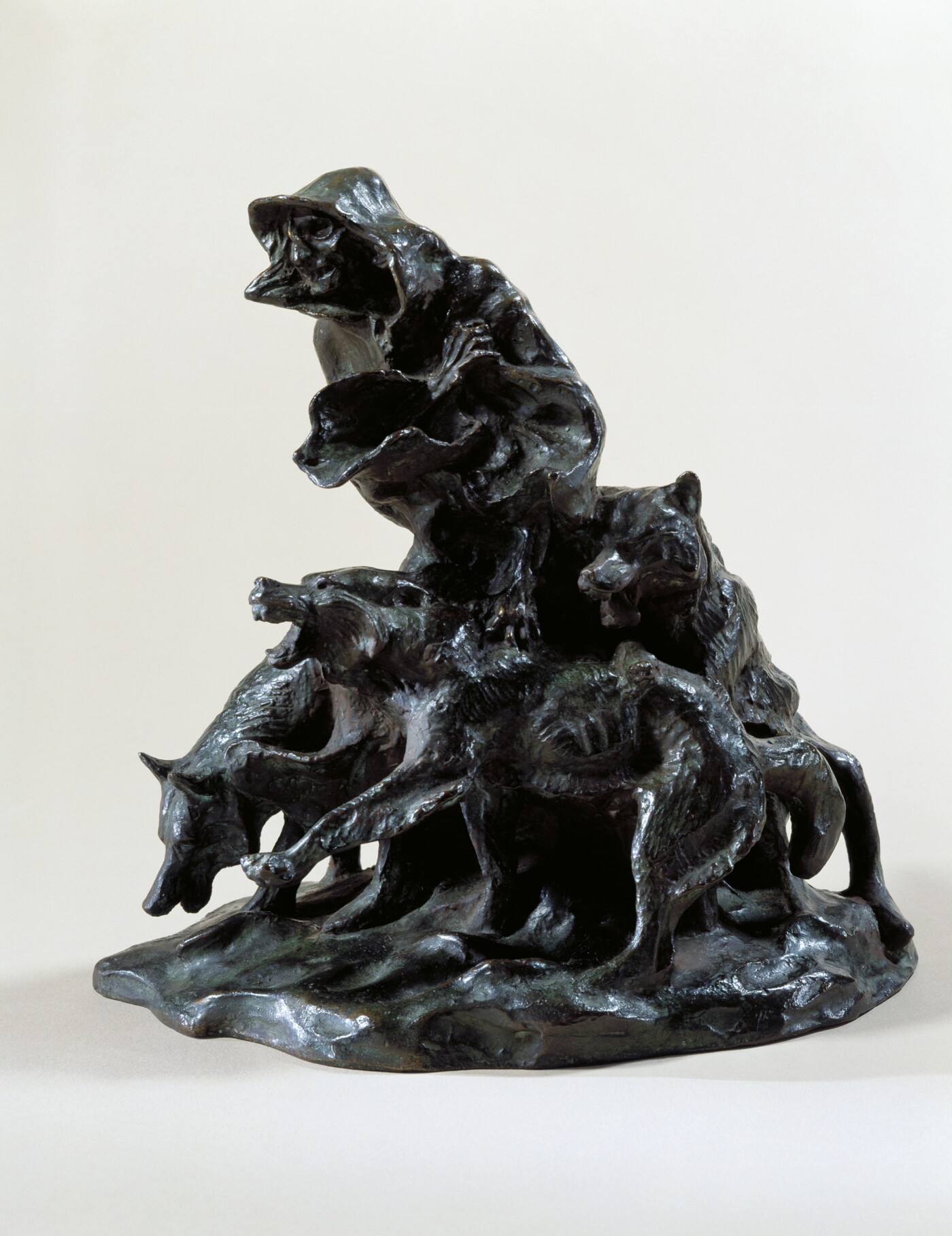 A bronze sculpture of an emaciated person wrapped in blankets surrounded by three snarling wolves.