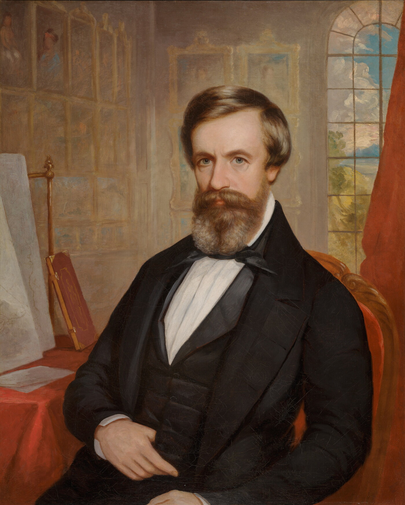 An oil painting of a White man with brown hair and beard wearing bow tie and jacket; artwork hangs salon-style on the walls behind him.
