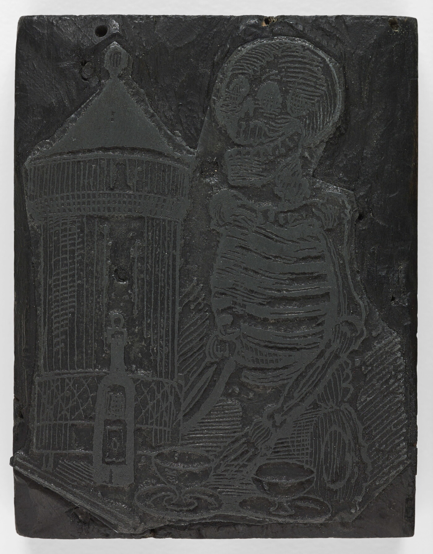 An engraved wood printing block depicting a skeleton standing in front of a table with a bottle and two glasses.