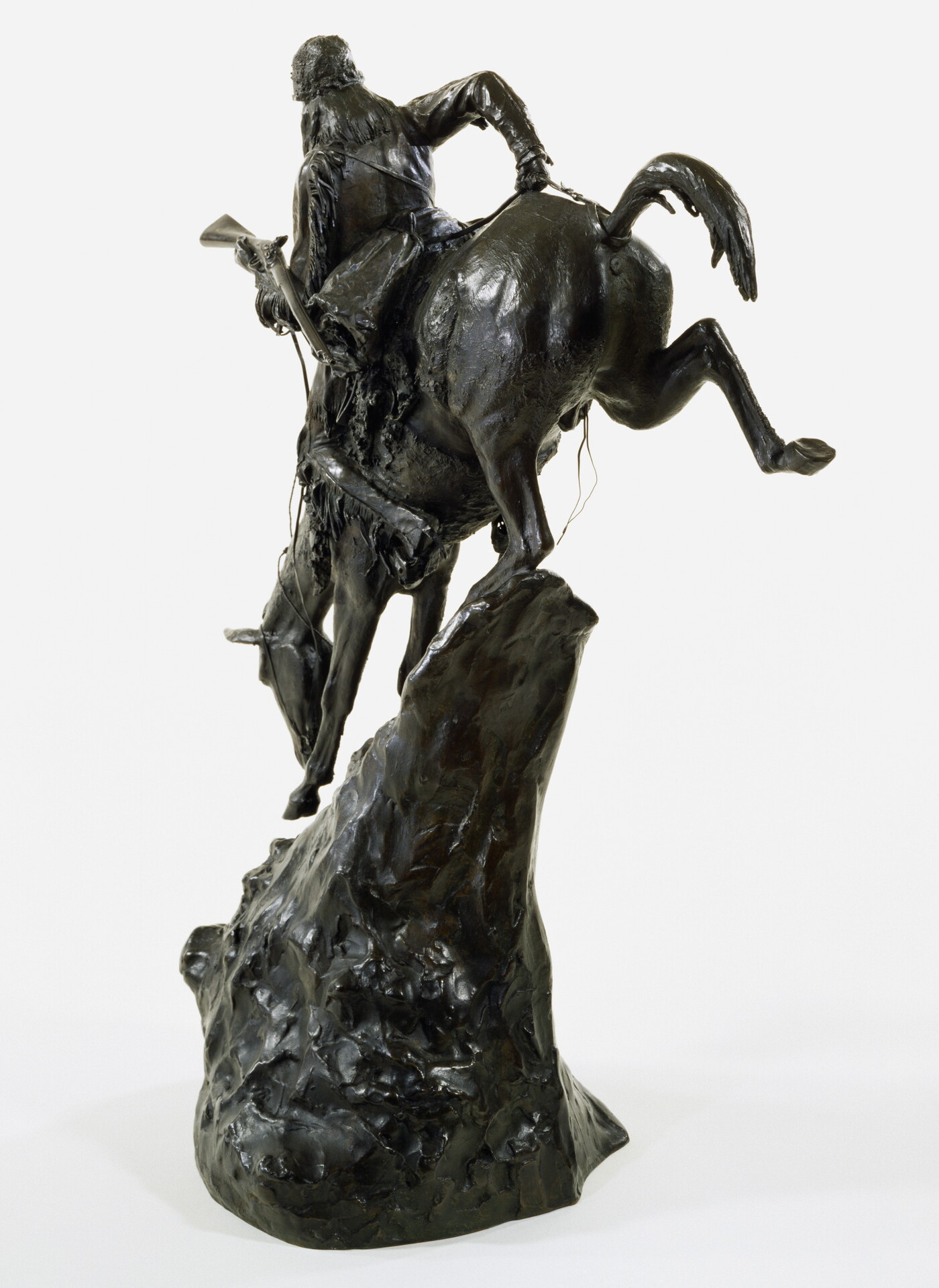 A bronze sculpture of an Indigenous man on horseback traveling down a steep mountain.