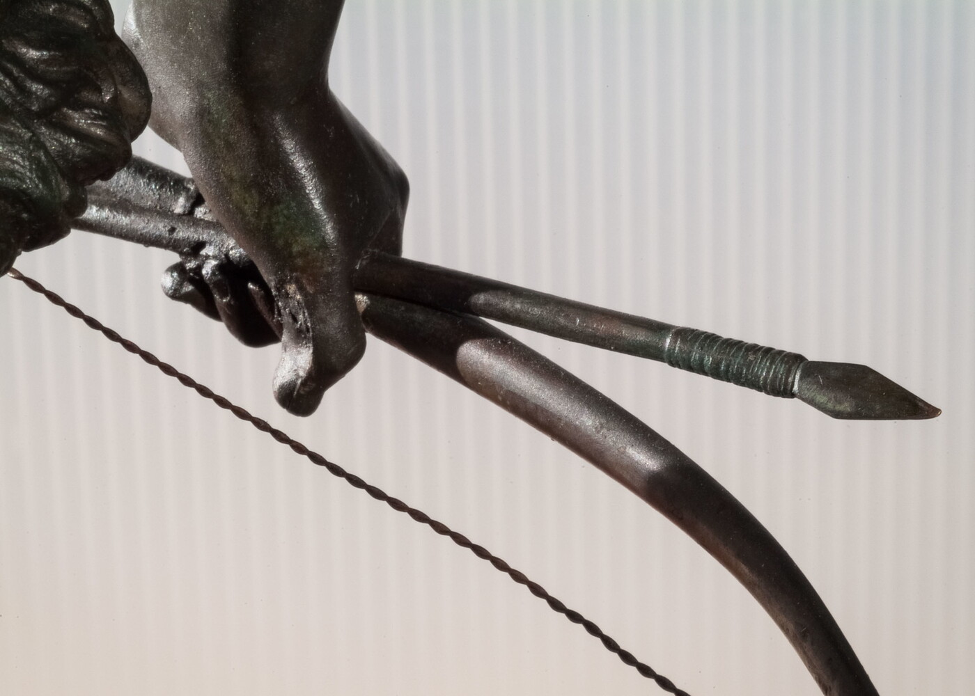 A detail of bronze sculpture of a young man holding a bow and arrow, standing hunched low with a dog beside him.