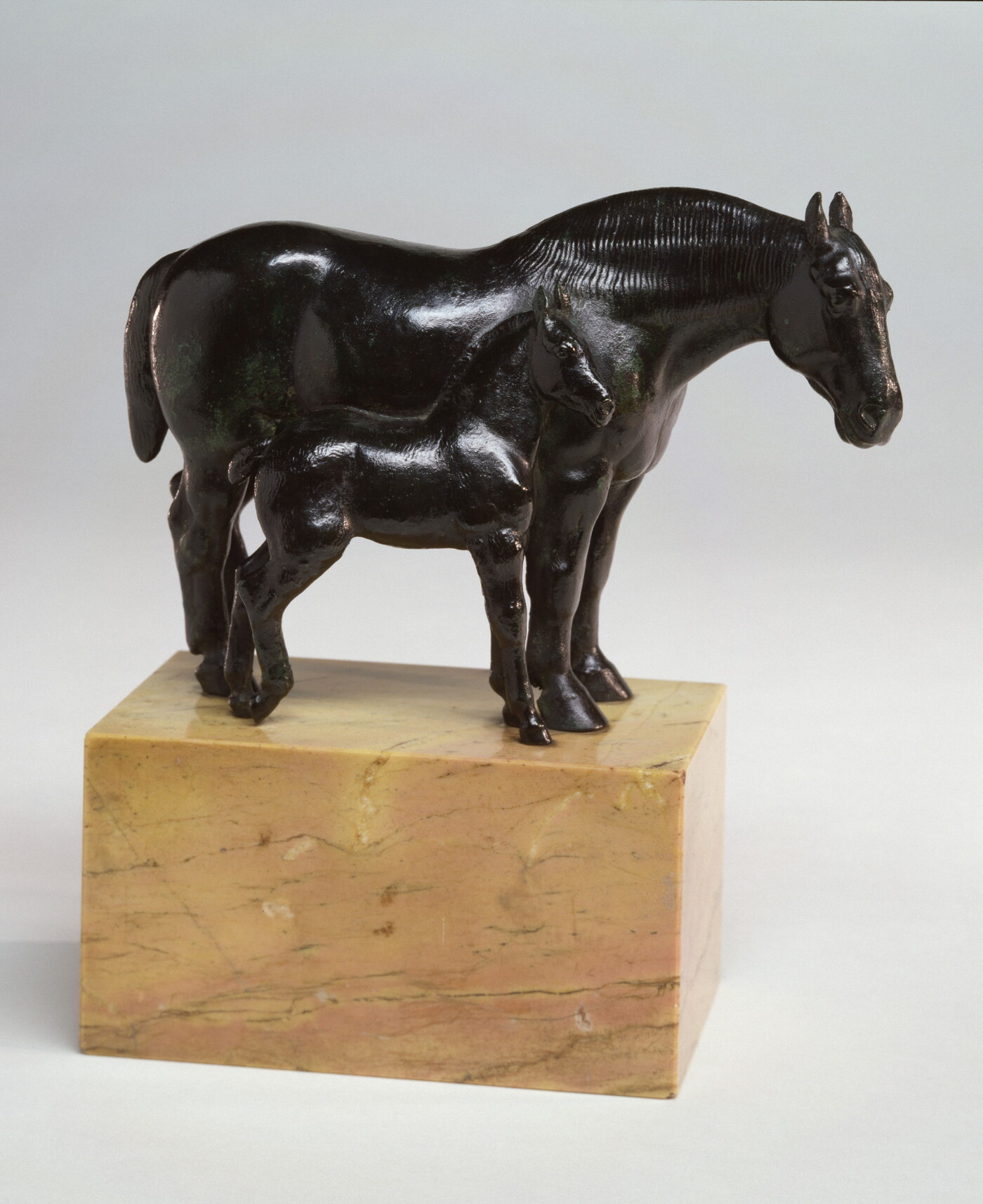 A bronze sculpture of two horses, a mare and a foal, standing next to each other on a stone base.