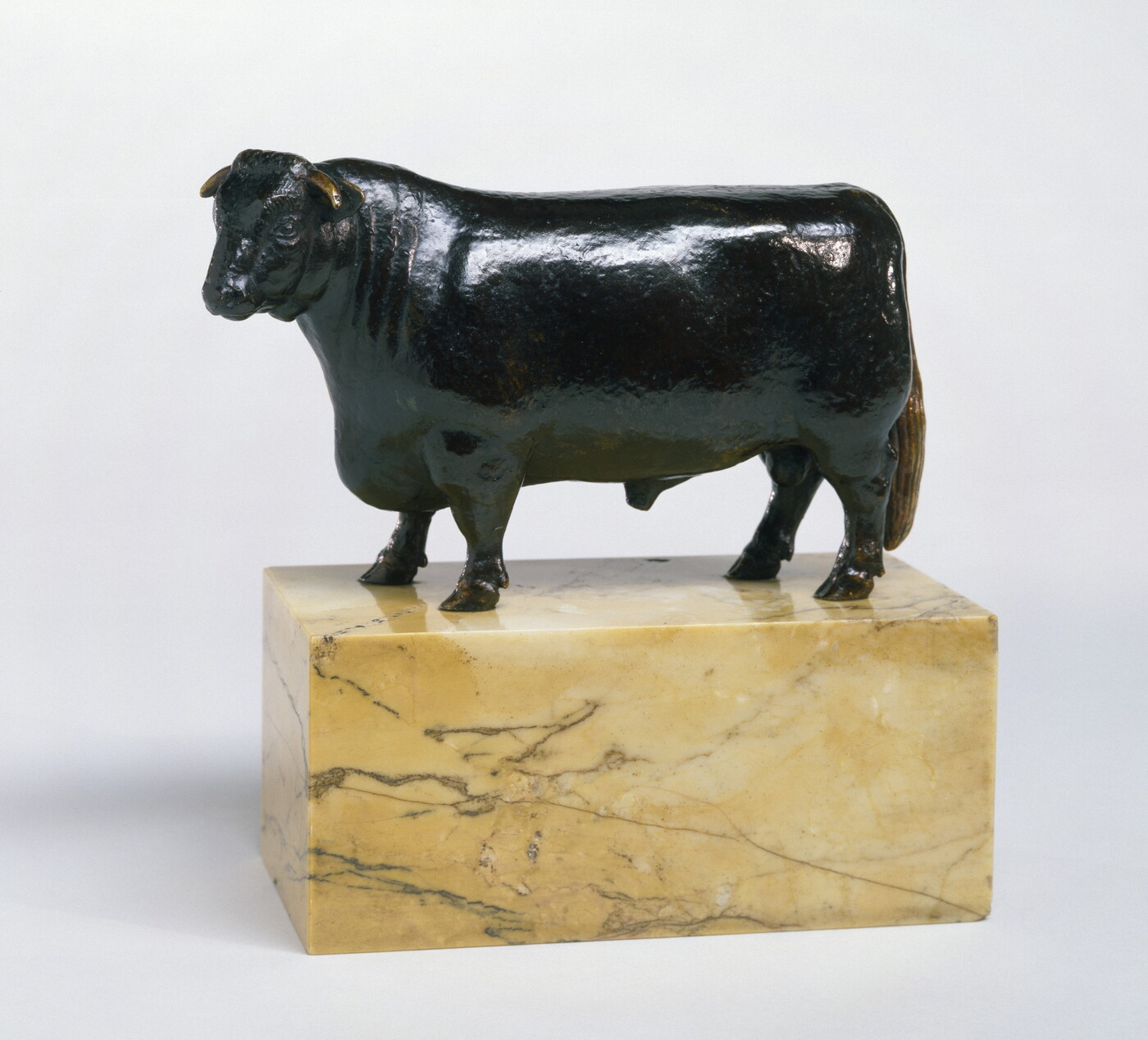 A bronze sculpture of a bull with a thick body and chest standing on a stone base.