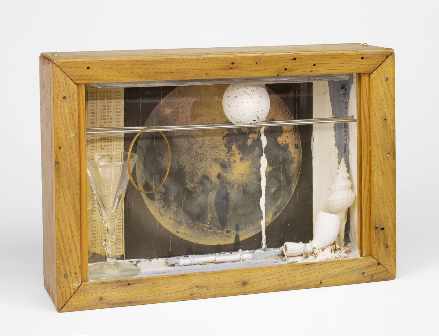 A wood shadowbox containing a pipe, a white ball with gray speckles, a picture of the moon, and a glass goblet.