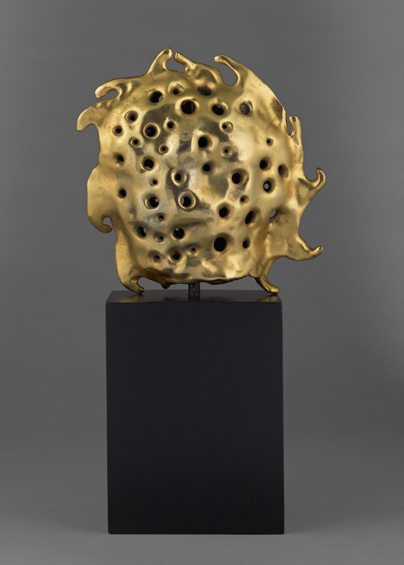 A bronze sculpture of a gold sun sitting atop a tall, dark rectangular base.