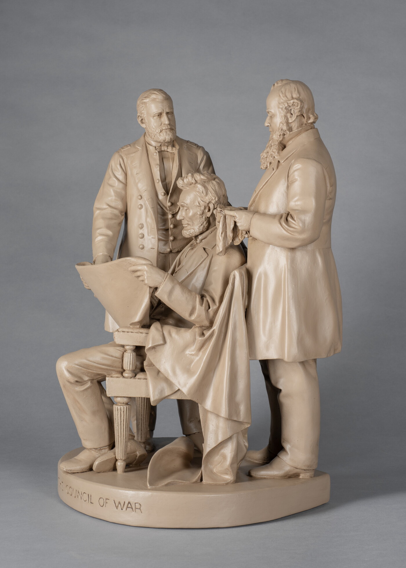 A sculpture of Abraham Lincoln reading a paper and seated in between two standing men.