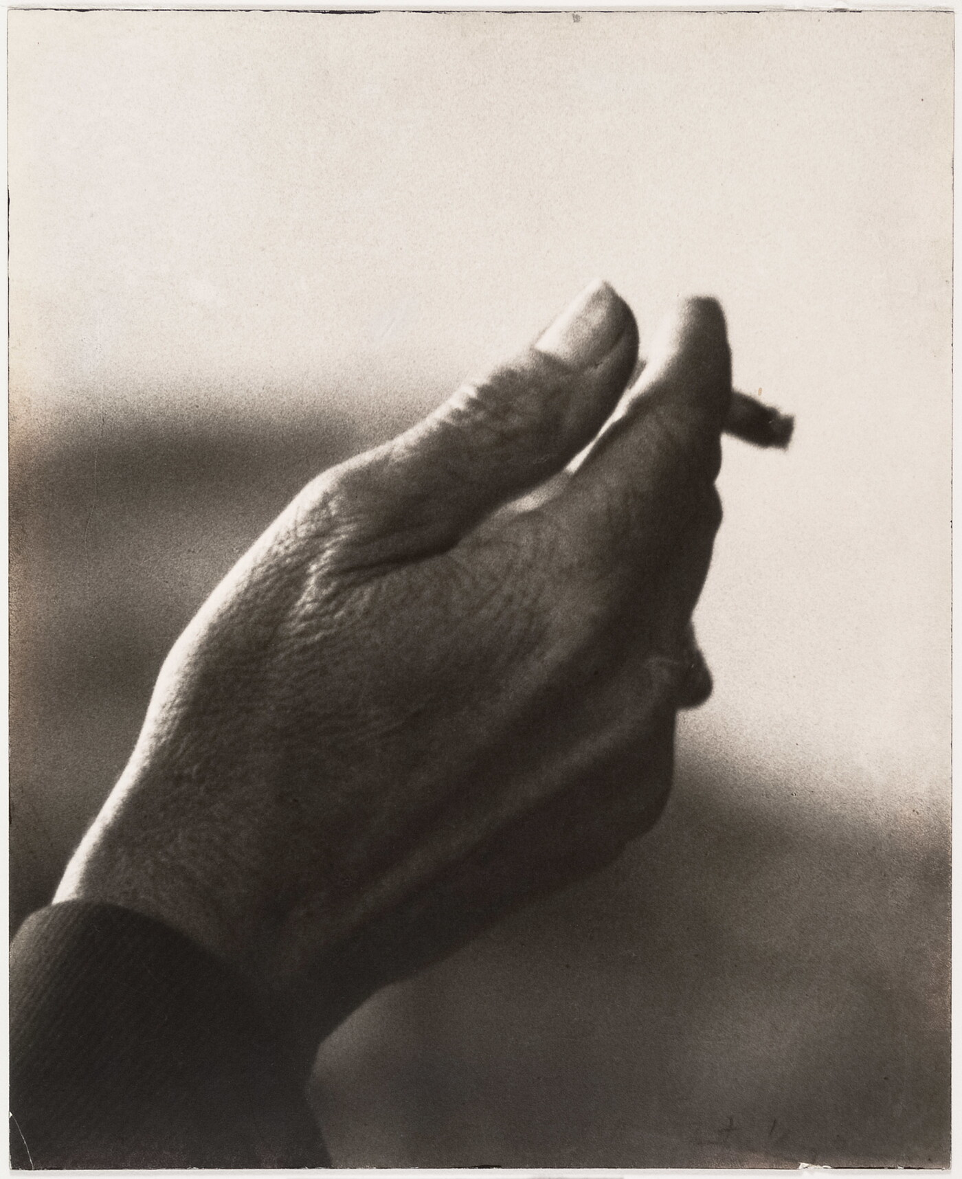 A sepia-toned close-up photograph of a right hand holding an almost-finished cigarette.
