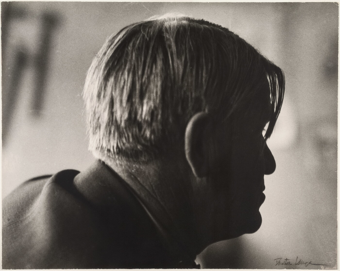 A sepia-toned photograph of a man's head in profile with longer pieces of hair hanging over his right eye.