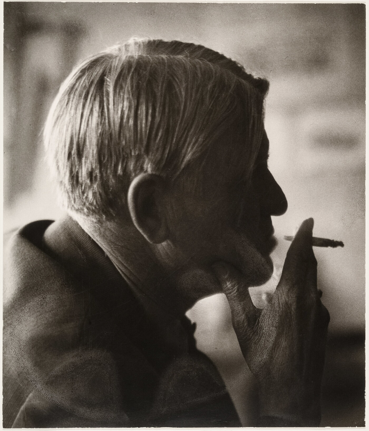 A sepia-toned photograph of a man's head in profile holding a cigarette posed in front of his lips.