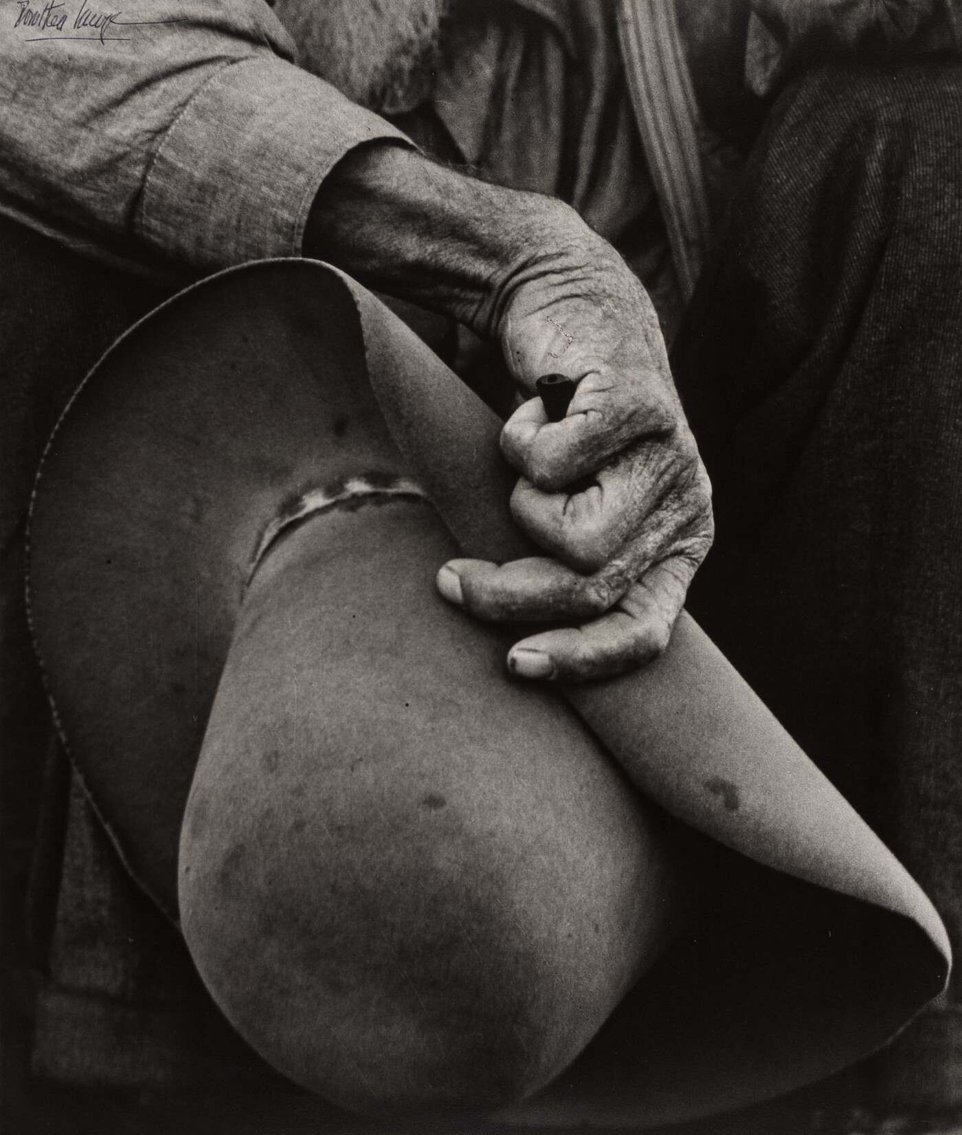 A close-up black-and-white photograph of a hand with aged, wrinkled skin holding a felt cowboy hat.