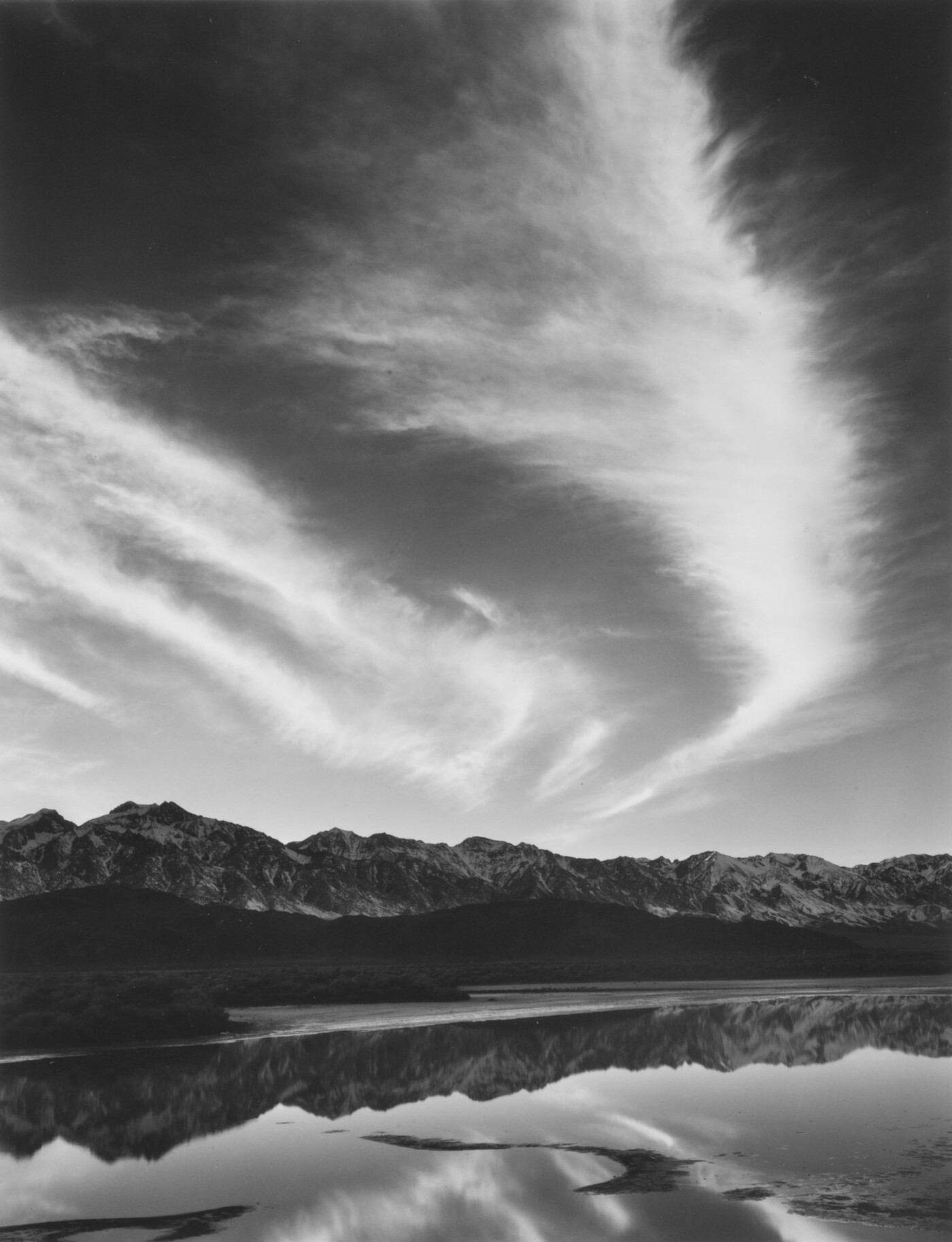 A black-and-white landscape photograph of mountains and clouds that reflect on the still water in the foreground.