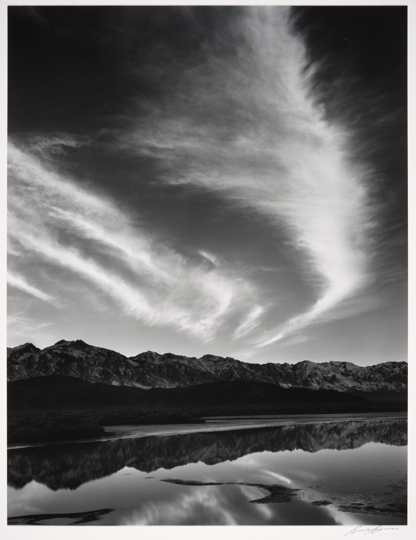 A black-and-white landscape photograph of mountains and clouds that reflect on the still water in the foreground.
