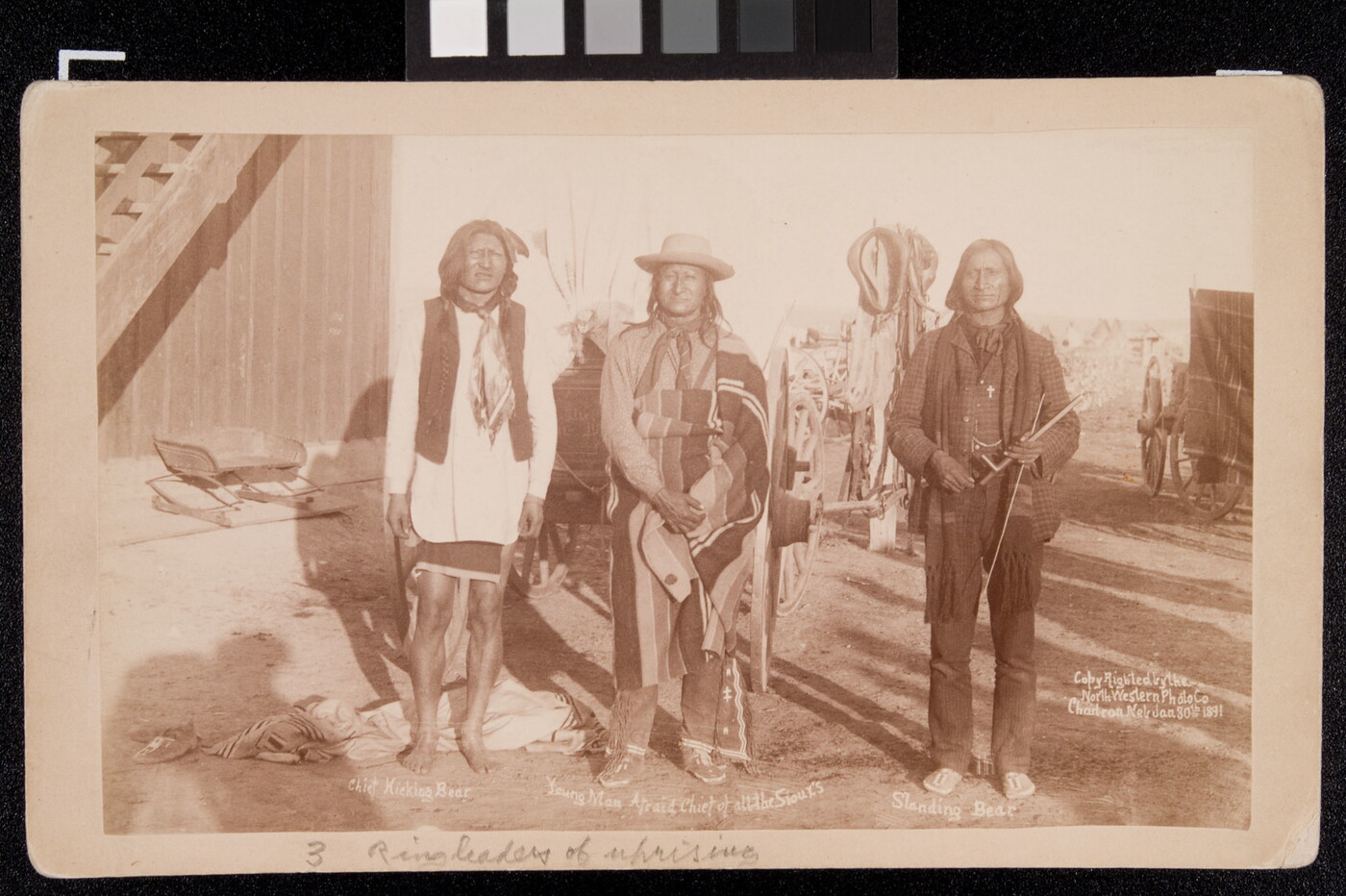 A sepia-toned photograph of three Indigenous men standing outside next to each other.