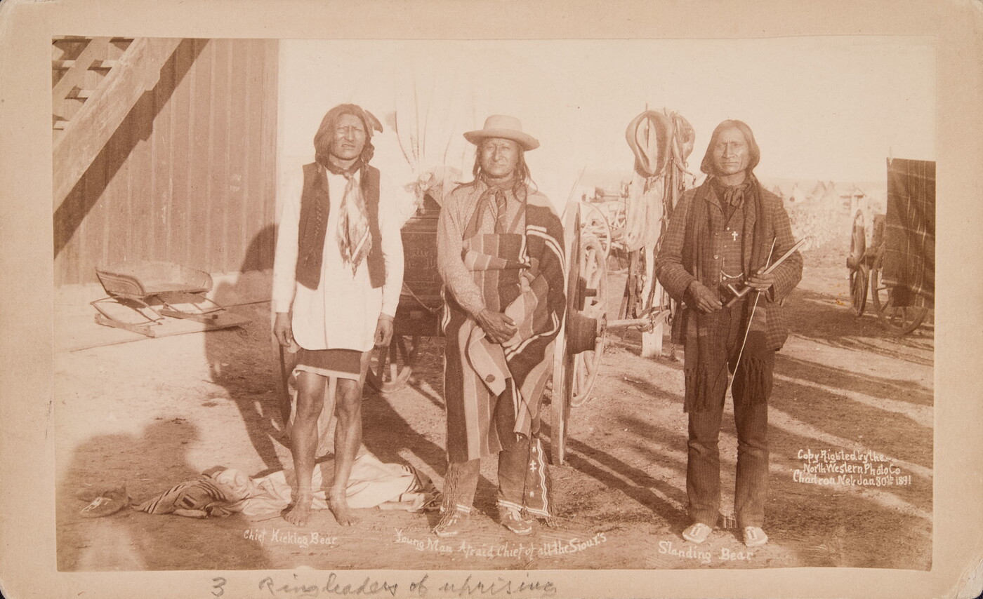 A sepia-toned photograph of three Indigenous men standing outside next to each other.