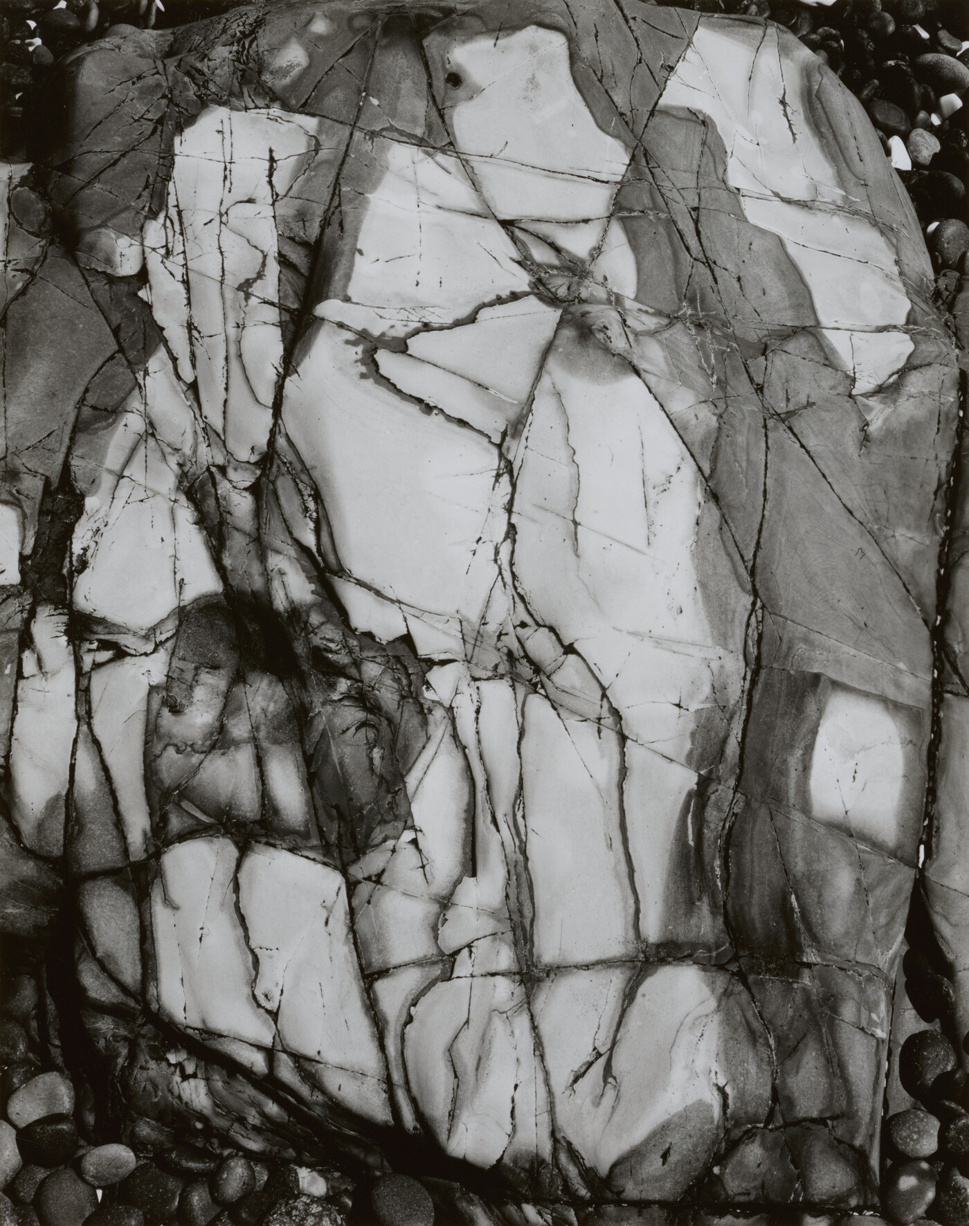 A black-and-white close-up photograph of a white rock with dark lines and cracks running through it.