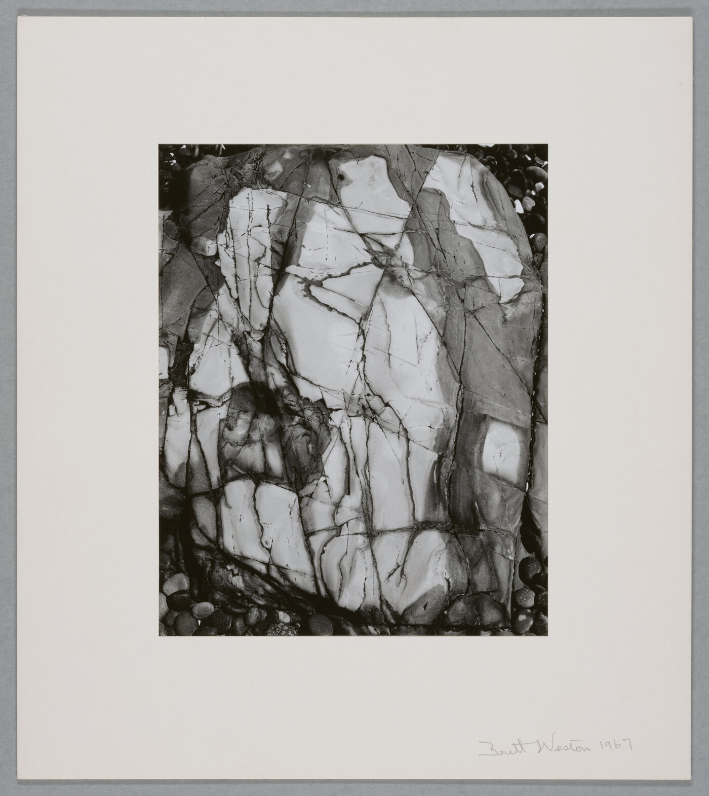 A black-and-white close-up photograph of a white rock with dark lines and cracks running through it.