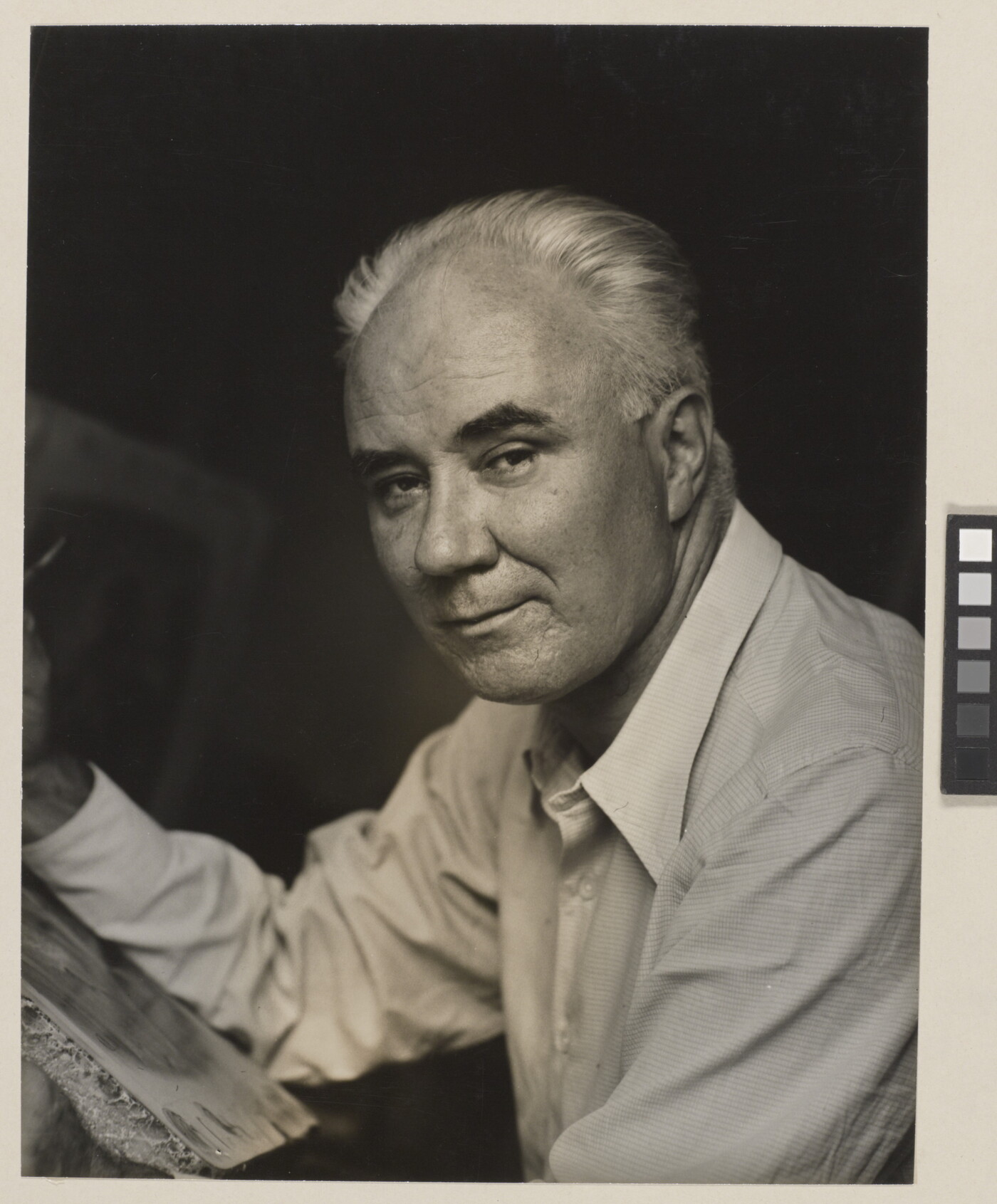 A black-and-white photograph of a middle-aged White man in three-quarter view leaning on something in front of him with his forearm.