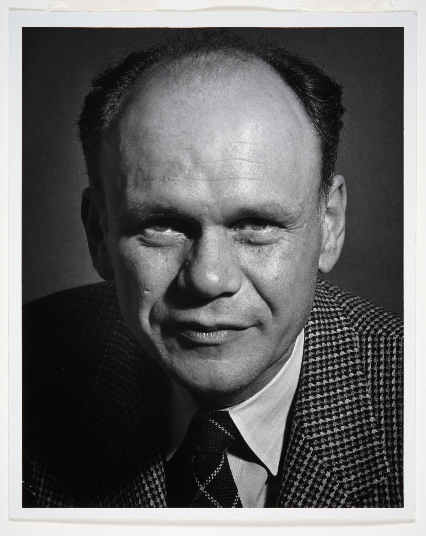 A black-and-white portrait photograph of a balding White man wearing a houndstooth blazer and striped tie.