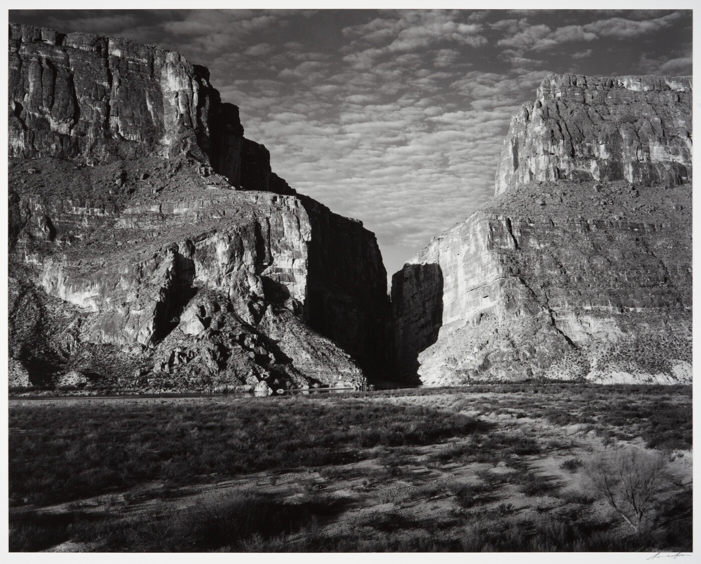A black-and-white photograph of a canyon between two large mountains.