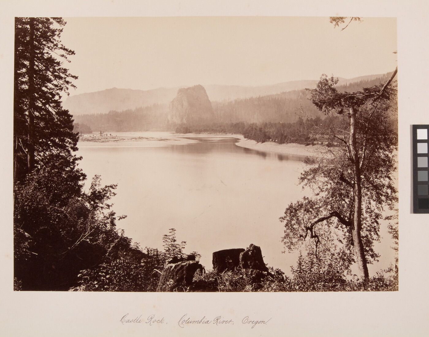 A sepia-toned photograph of a serene river surrounded by trees, rock formations, and mountains.