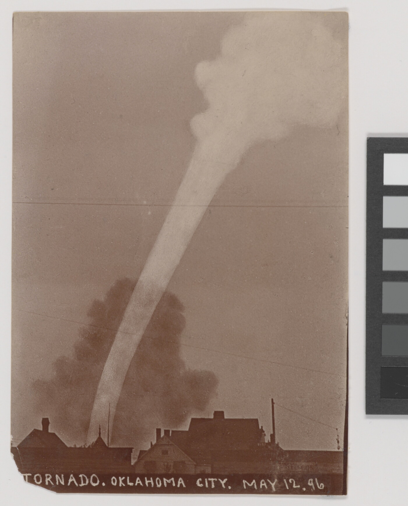 A sepia-toned photograph of a white funnel cloud above the silhouette of a town.