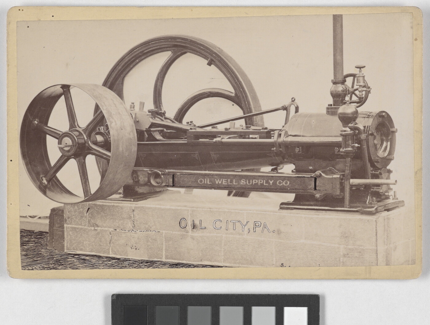 A black-and-white photograph of a machine with two wheels of varying sizes sitting on a concrete base.
