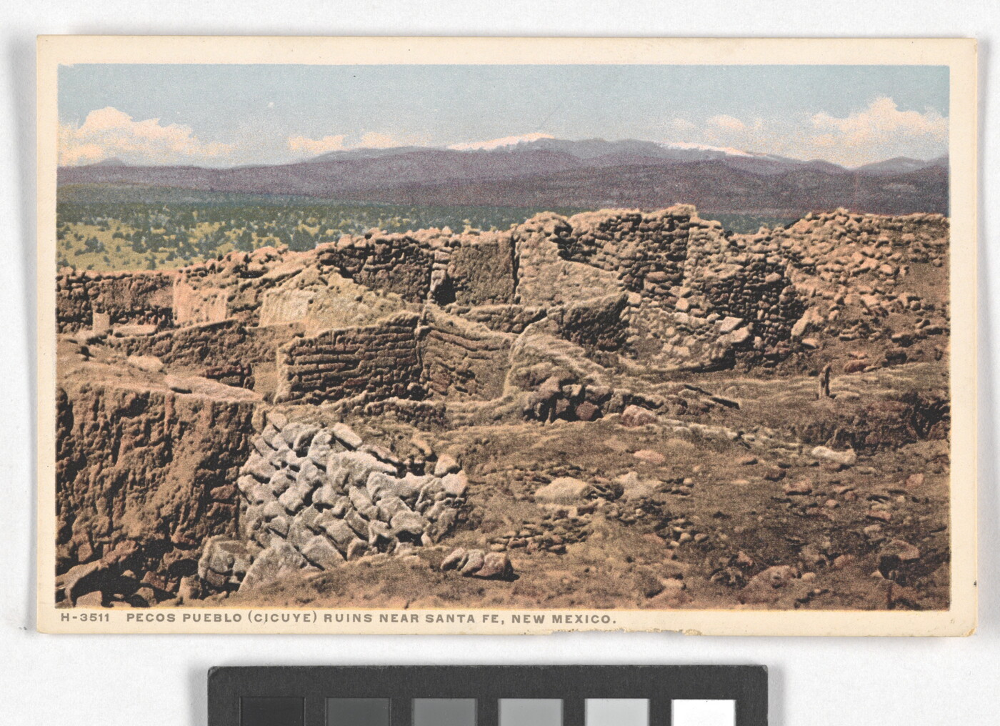 A color postcard of a ruined, stone building with multiple rooms in a mountainous landscape.