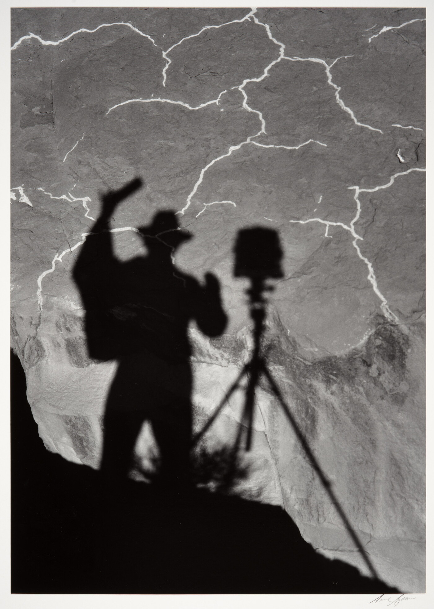 A black-and-white photograph of the shadow of a person and tripod with camera cast from above onto the landscape below.