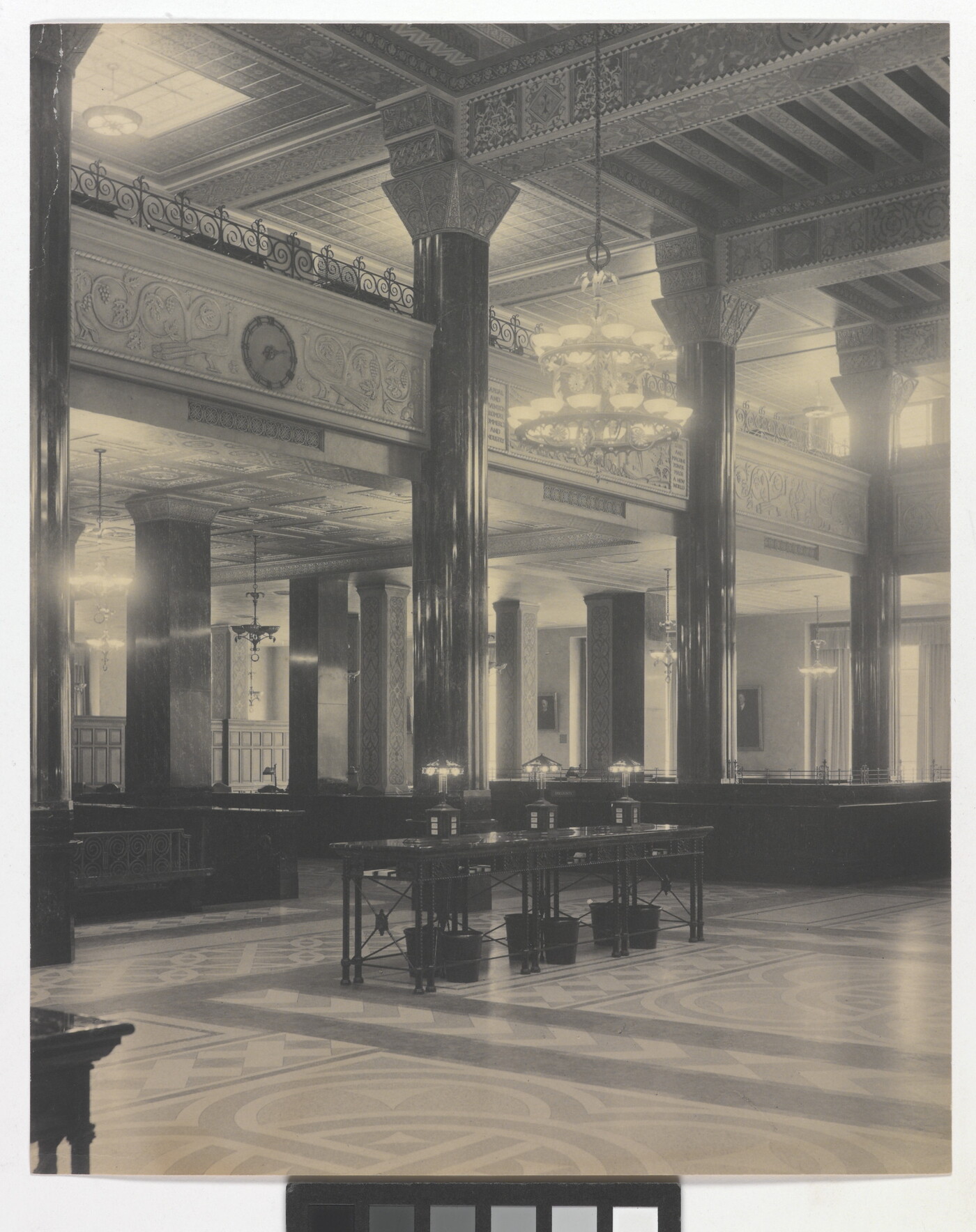 A black-and-white photograph of the interior of an ornate office lobby with inlaid floors, columns, and chandeliers.