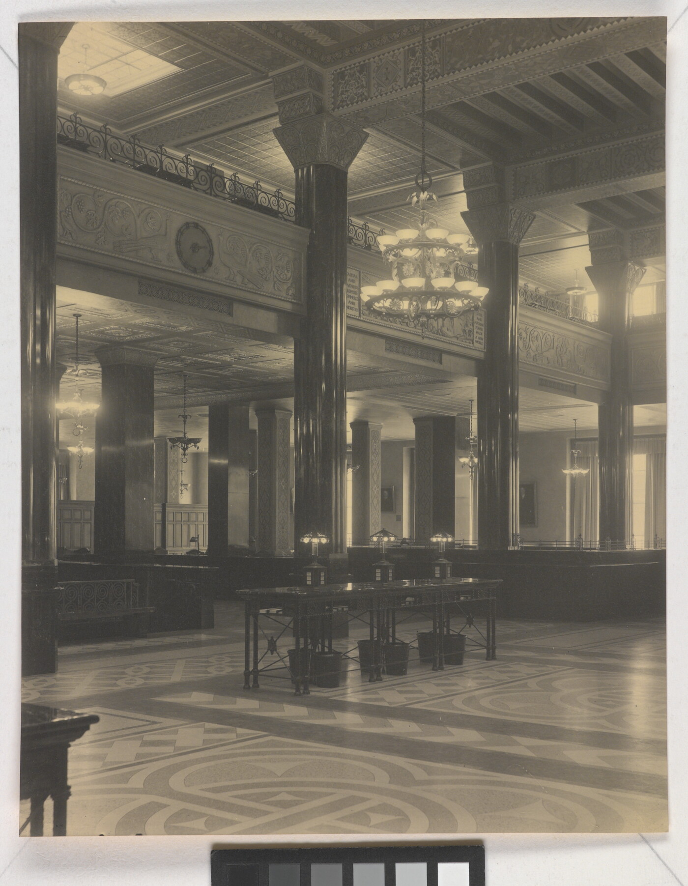 A black-and-white photograph of the interior of an ornate office lobby with inlaid floors, columns, and chandeliers.