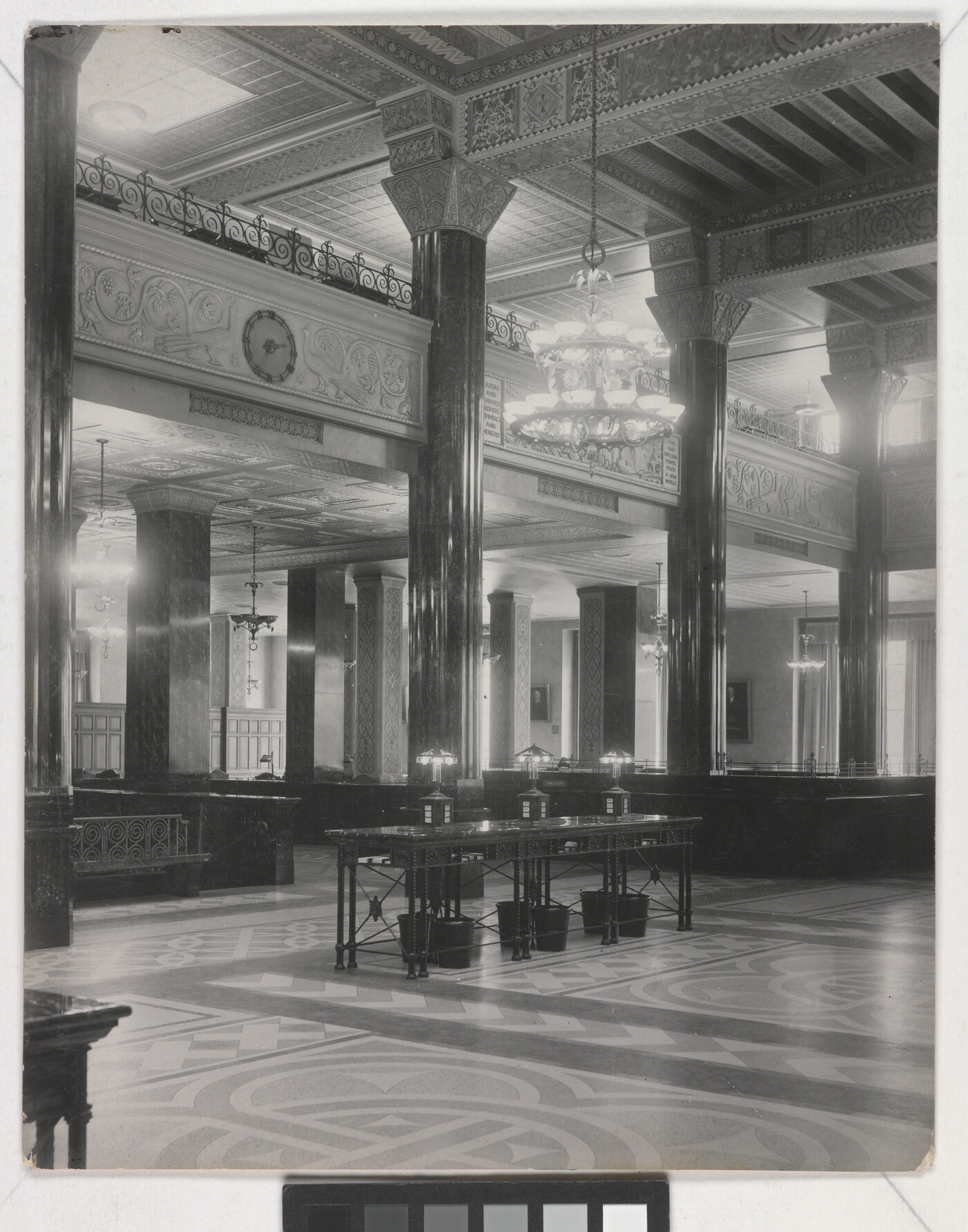 A black-and-white photograph of the interior of an ornate office lobby with inlaid floors, columns, and chandeliers.