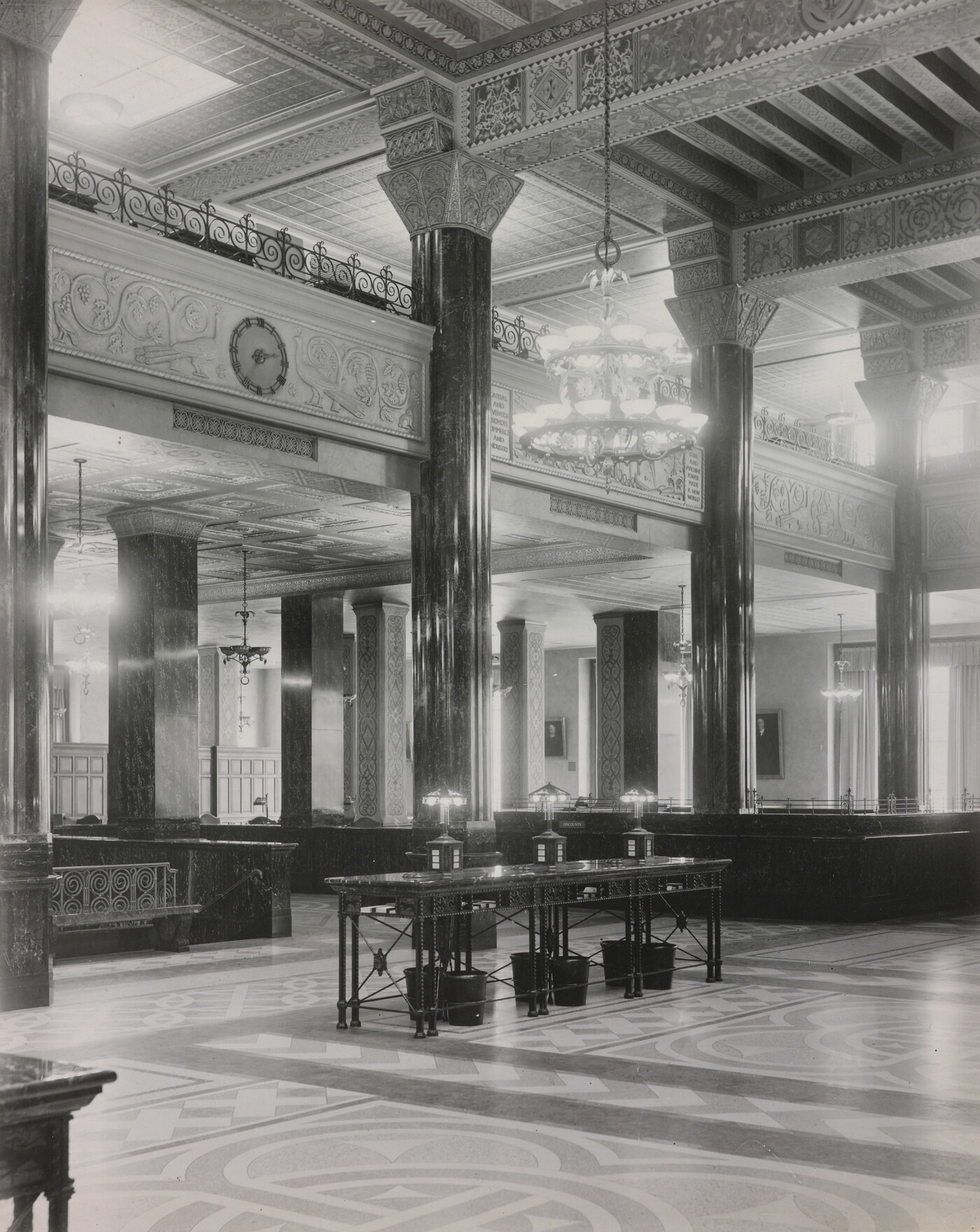 A black-and-white photograph of the interior of an ornate office lobby with inlaid floors, columns, and chandeliers.