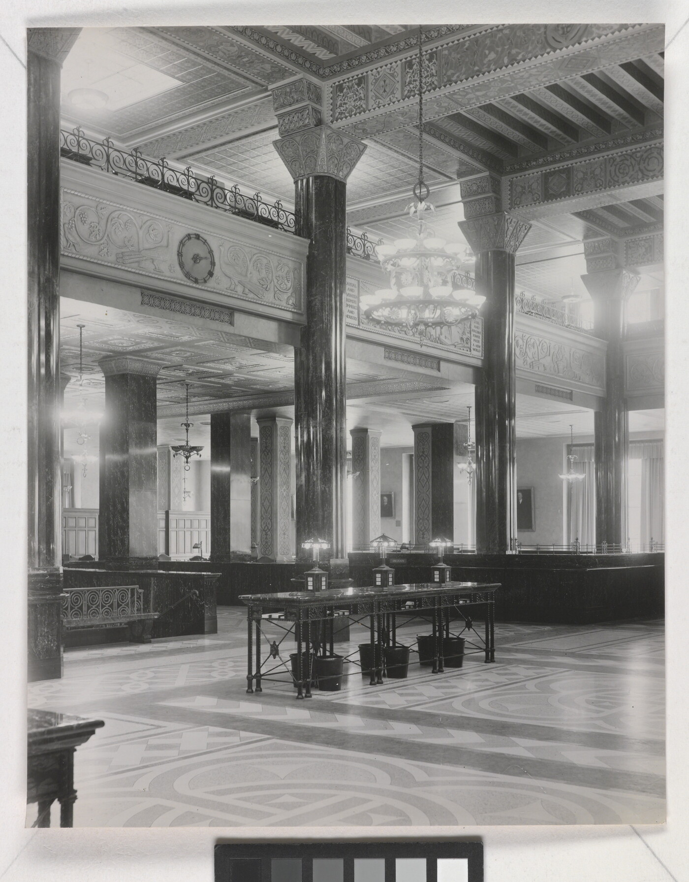 A black-and-white photograph of the interior of an ornate office lobby with inlaid floors, columns, and chandeliers.