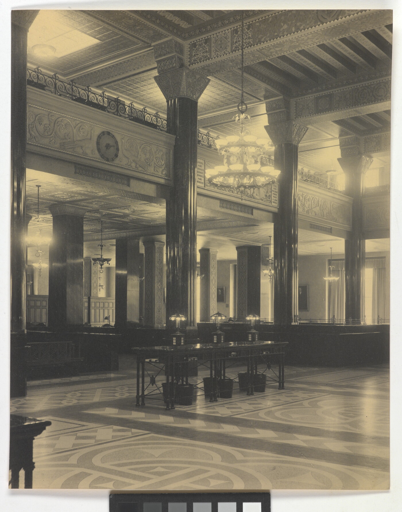 A black-and-white photograph of the interior of an ornate office lobby with inlaid floors, columns, and chandeliers.